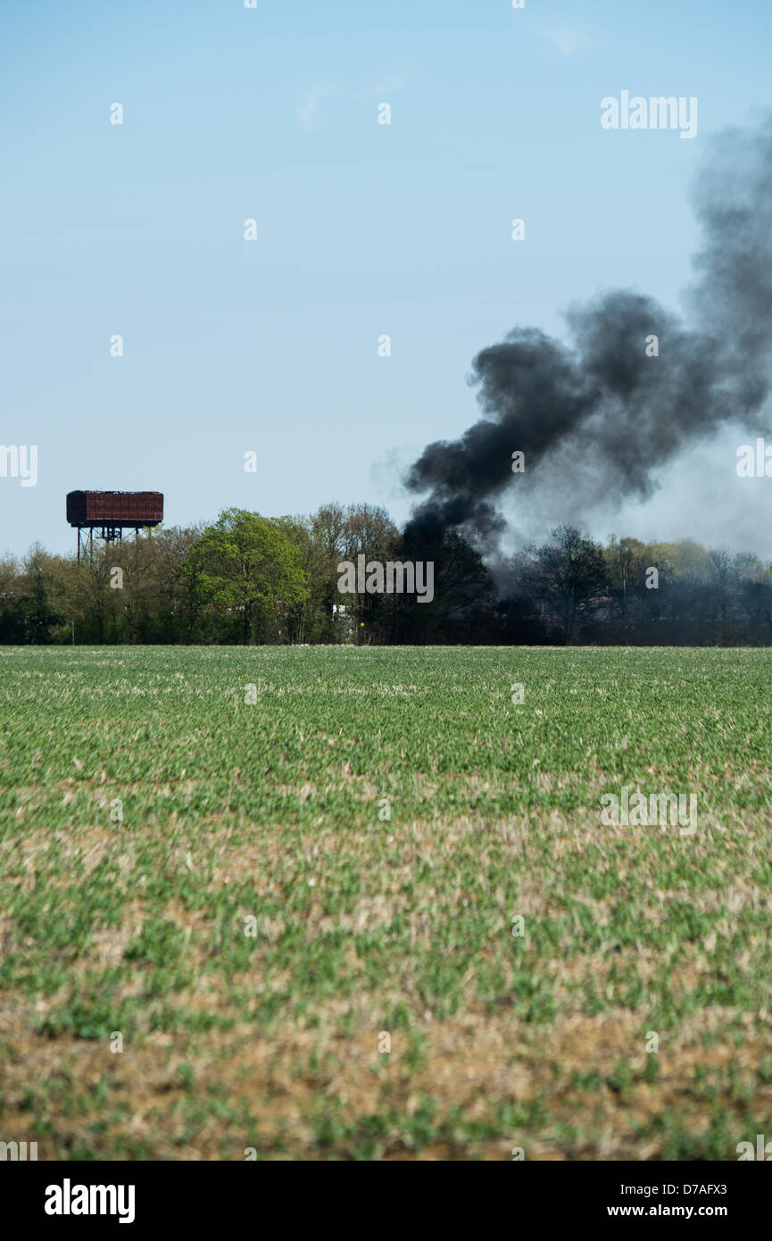 Fumo nero sorge in un cielo blu da un incendio in un vecchio campo d'aviazione in Essex come una pila di gomme bruciano. Foto Stock