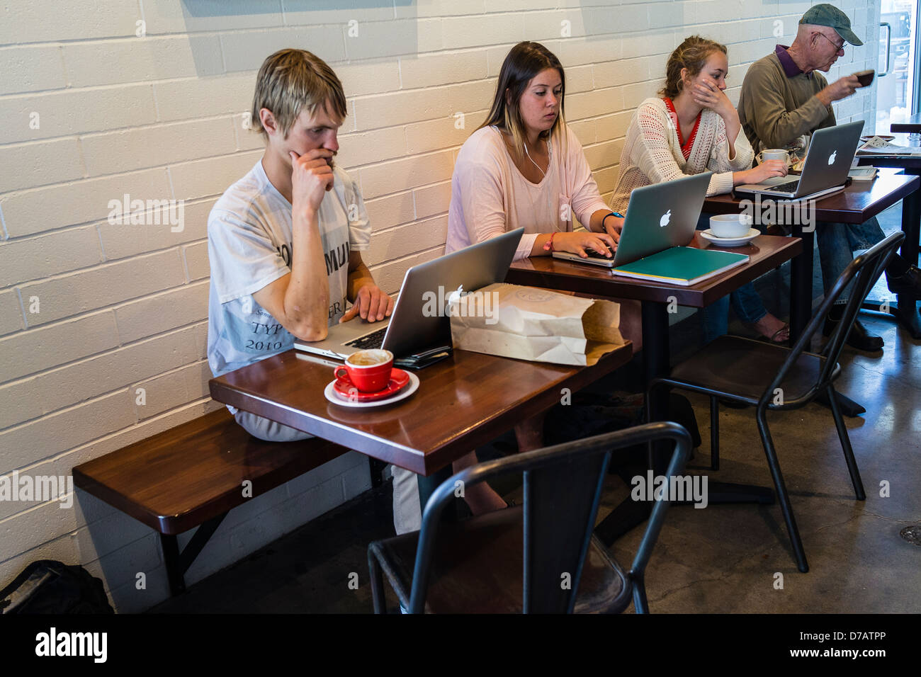 Linea Giovane fino a una tavola utilizzando i loro computer portatili Apple in un bar locale. Sullo sfondo di un adulto più anziano beve caffè. Foto Stock