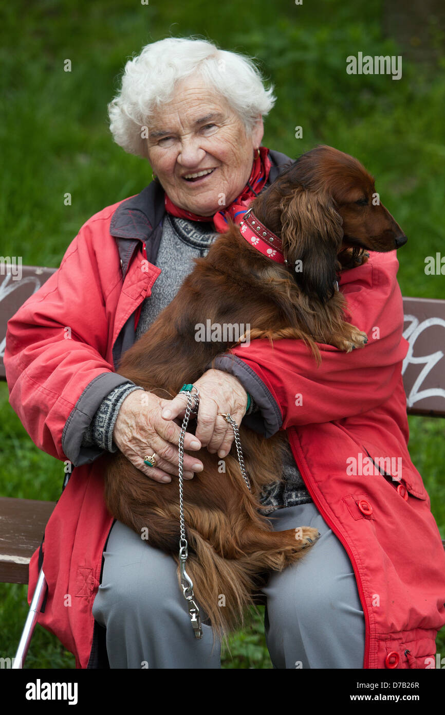 Una donna anziana con un cane su una panchina, anziana donna anziana, anziana donna cane, abbraccio 70s in pensione, pensionato su una panchina da giardino cane donna anziana Foto Stock