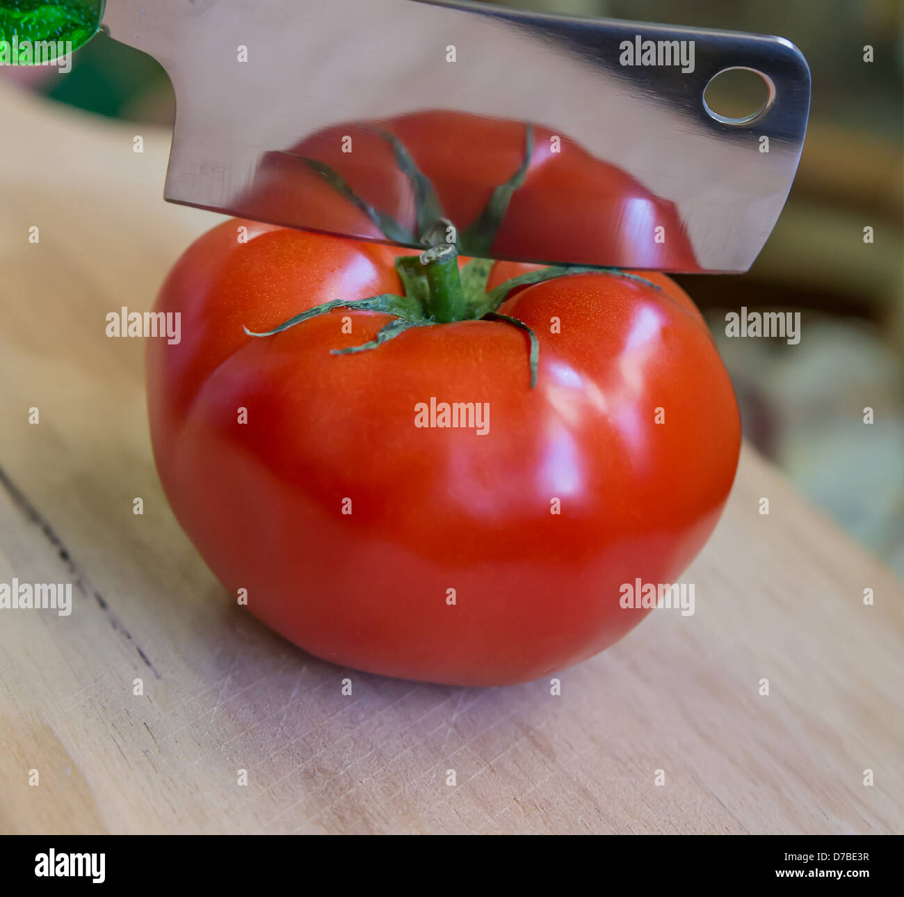 Un pomodoro pronto per essere tagliato a metà con un cleaver. Il pomodoro è riflettente per la cleaver Foto Stock