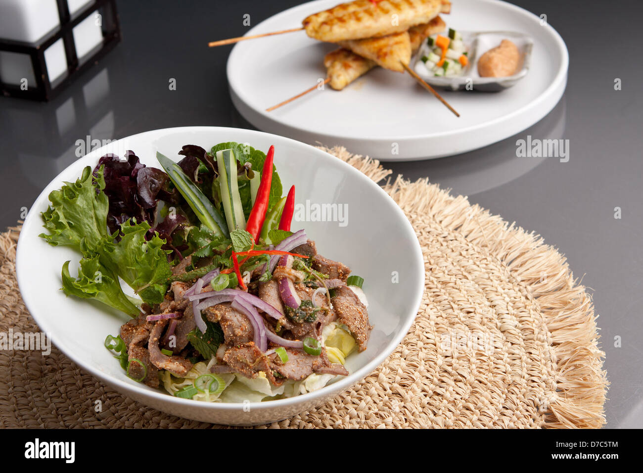 Stile asiatico insalata Thai con manzo e pollo satay di pollo alla brace su spiedini antipasti in background. Foto Stock