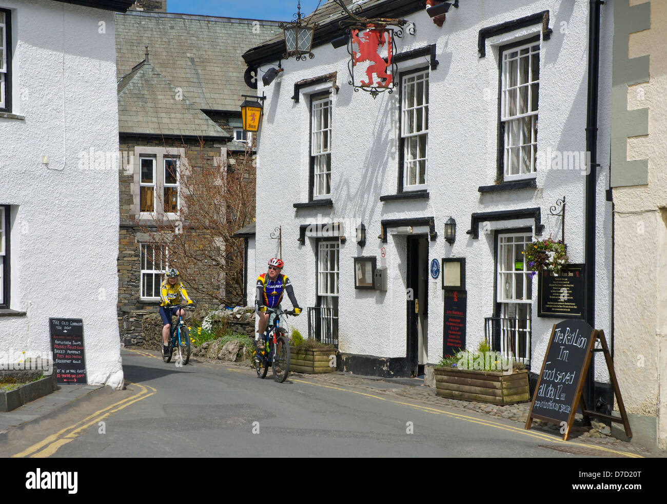 Due ciclisti passando il Red Lion Inn, Hawkshead, Parco Nazionale del Distretto dei Laghi, Cumbria, England Regno Unito Foto Stock