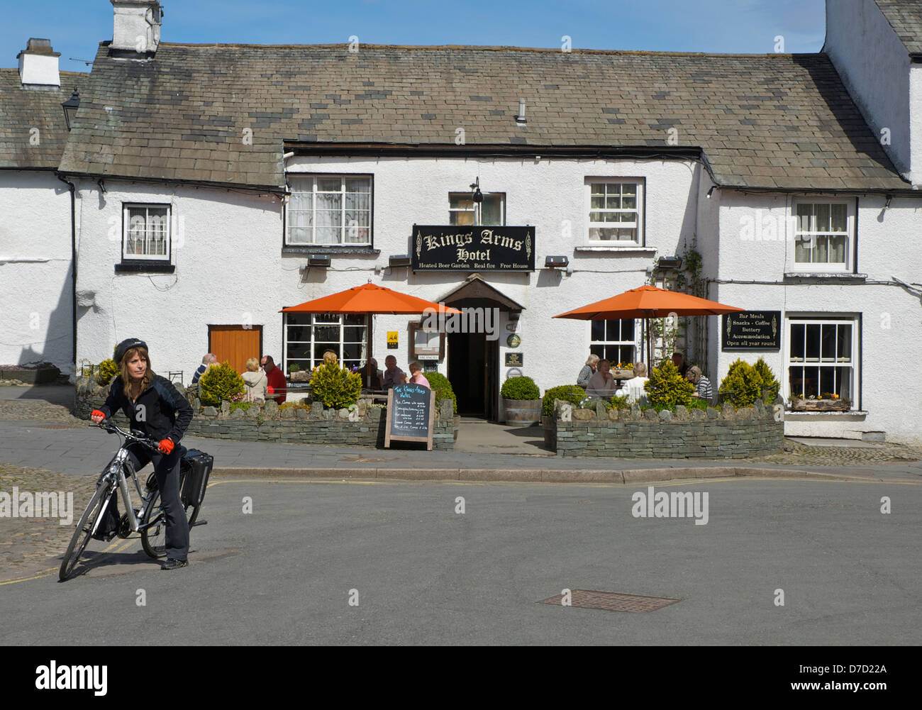 Giovane donna in sella della bicicletta elettrica nel villaggio di Hawkshead, Parco Nazionale del Distretto dei Laghi, Cumbria, England Regno Unito Foto Stock