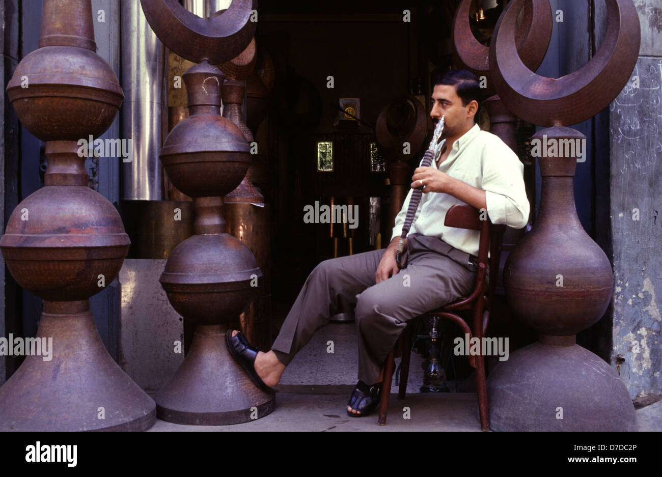Un uomo egiziano che fuma pipa di narghilè in un negozio che vende pietre di rame a mezzaluna simbolo dell'Islam a Khan el-Khalili, un importante suk nel centro storico del Cairo islamico in Egitto Foto Stock