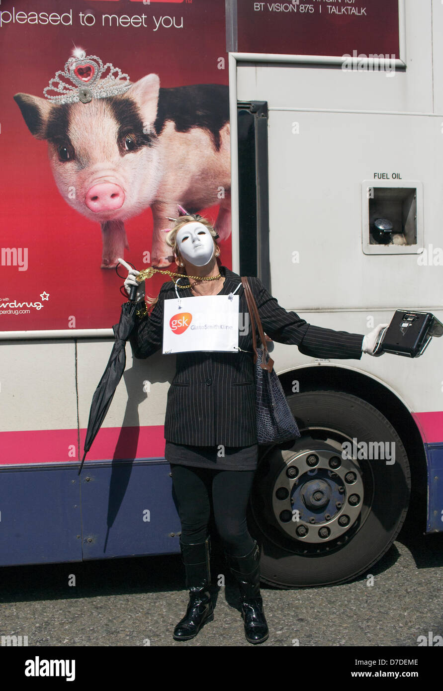 Bristol,UK,4 Maggio,2013. Una donna protester indossa una maschera facciale bianca e portante una cassa pone accanto a un annuncio su un bus di passaggio che mostra la foto di un maiale come lei prende parte a manifestazioni di protesta contro la privatizzazione del NHS. Credito: lynchpics / Alamy Live News Foto Stock