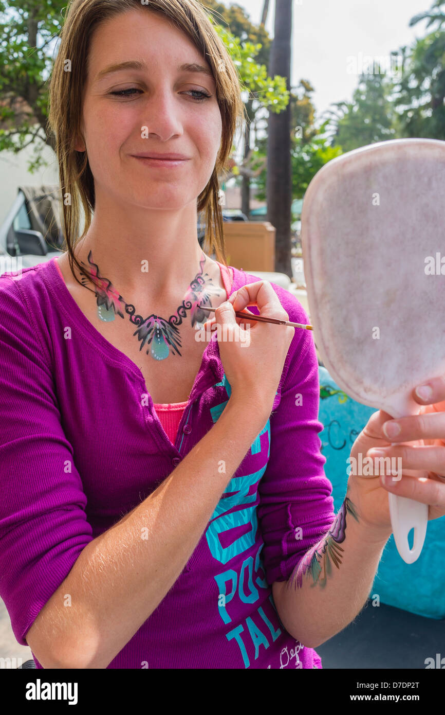 Un 20-29 anno vecchio volto femminile e il corpo pittore dimostra le sue abilità di pittura con la pittura con una spazzola sul suo torace superiore. Foto Stock