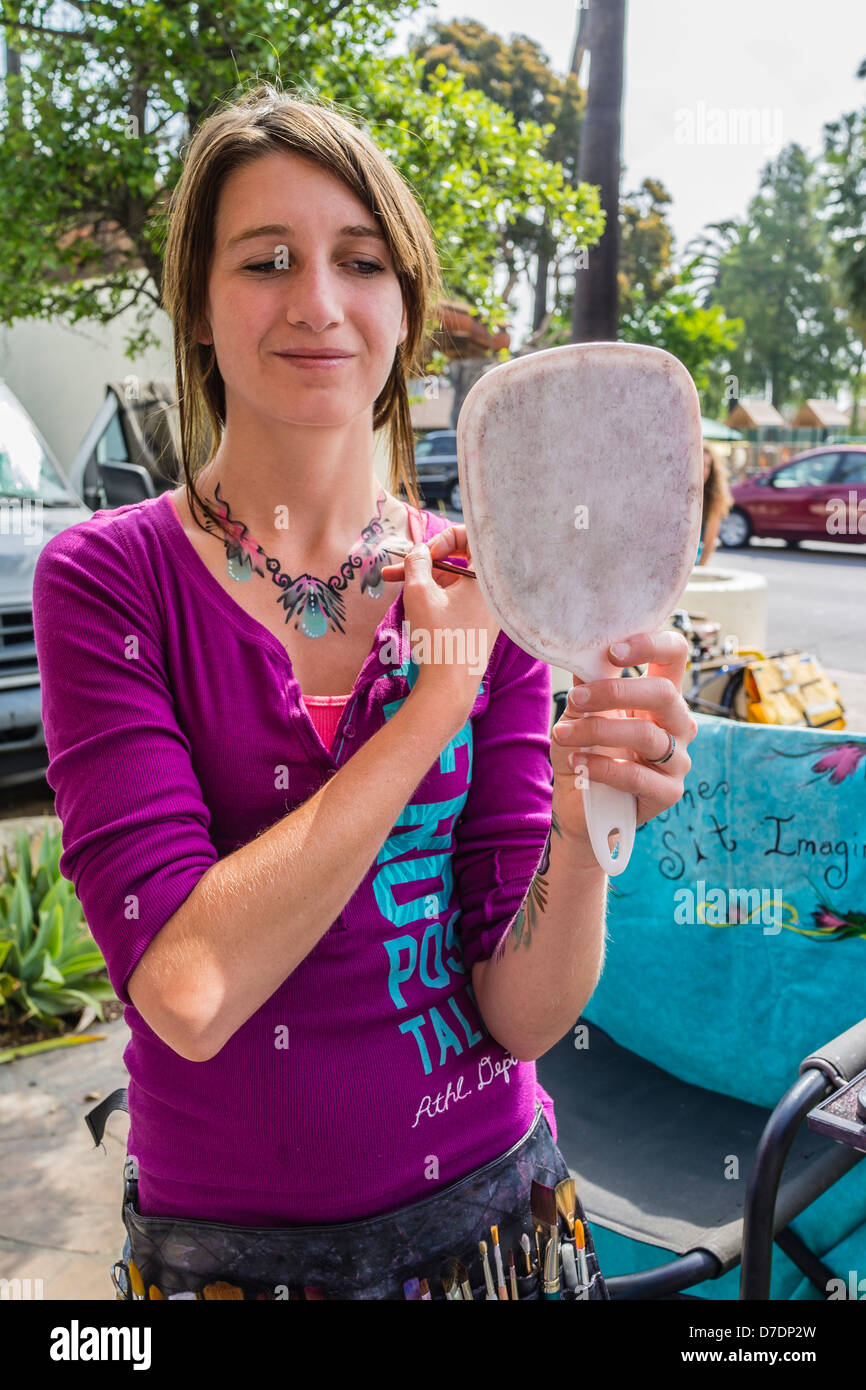Un 20-29 anno vecchio volto femminile e il corpo pittore dimostra le sue abilità di pittura con la pittura con una spazzola sul suo torace superiore. Foto Stock