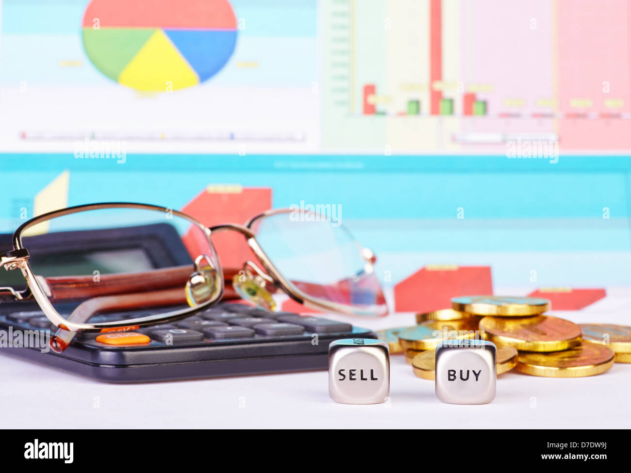Dadi a cubetti con le parole comprare vendere, monete d'oro, calcolatrice,bicchieri e schemi finanziari come sfondo. Messa a fuoco selettiva Foto Stock