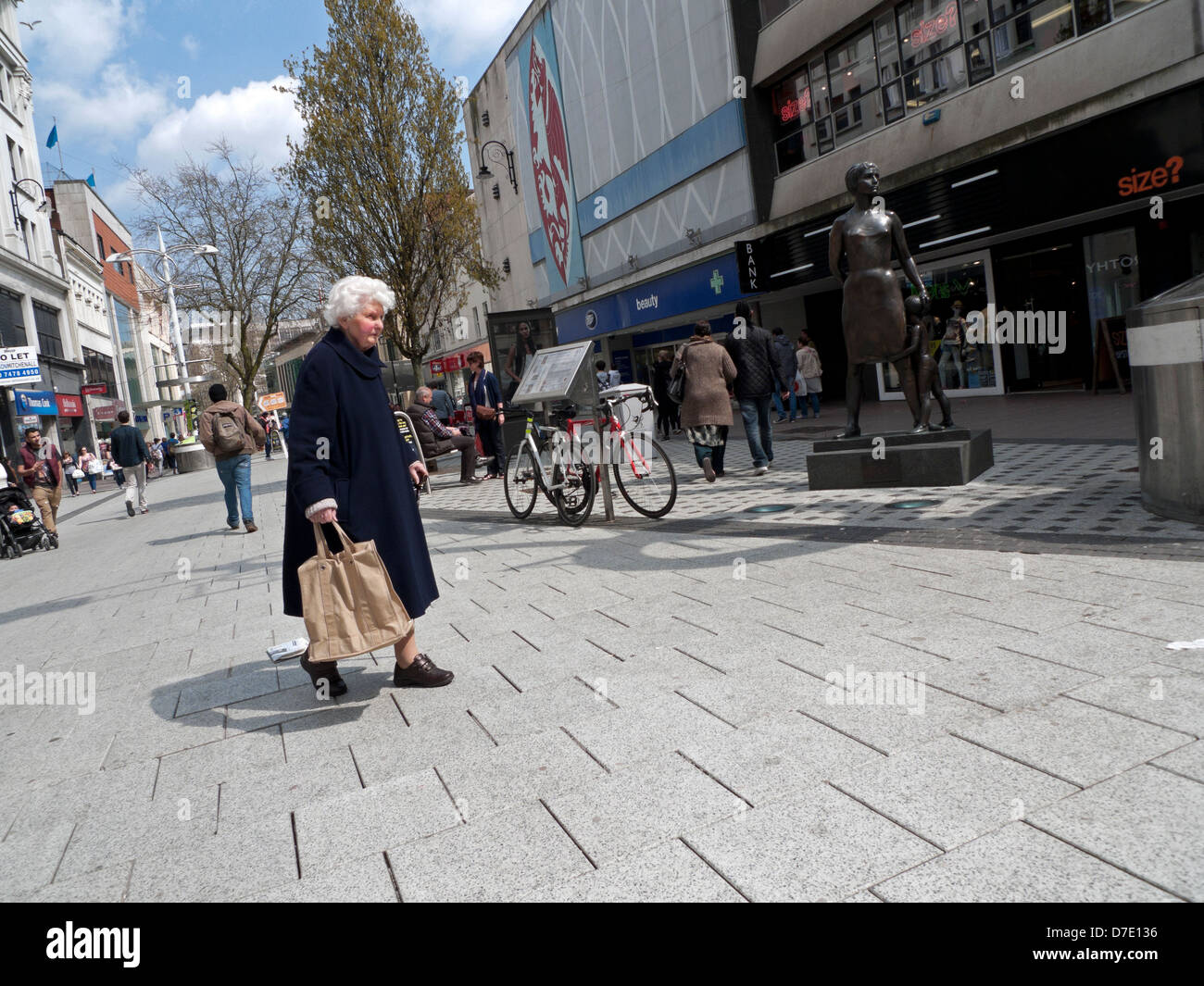 Donna anziana con un carrello indietro a piedi in Queen Street Cardiff City Centre Wales UK Foto Stock