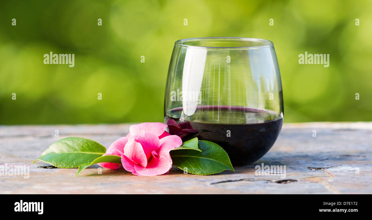 Foto orizzontale di vino rosso in vetro e in tarda primavera fiore rosa con Brillante sfondo verde Foto Stock