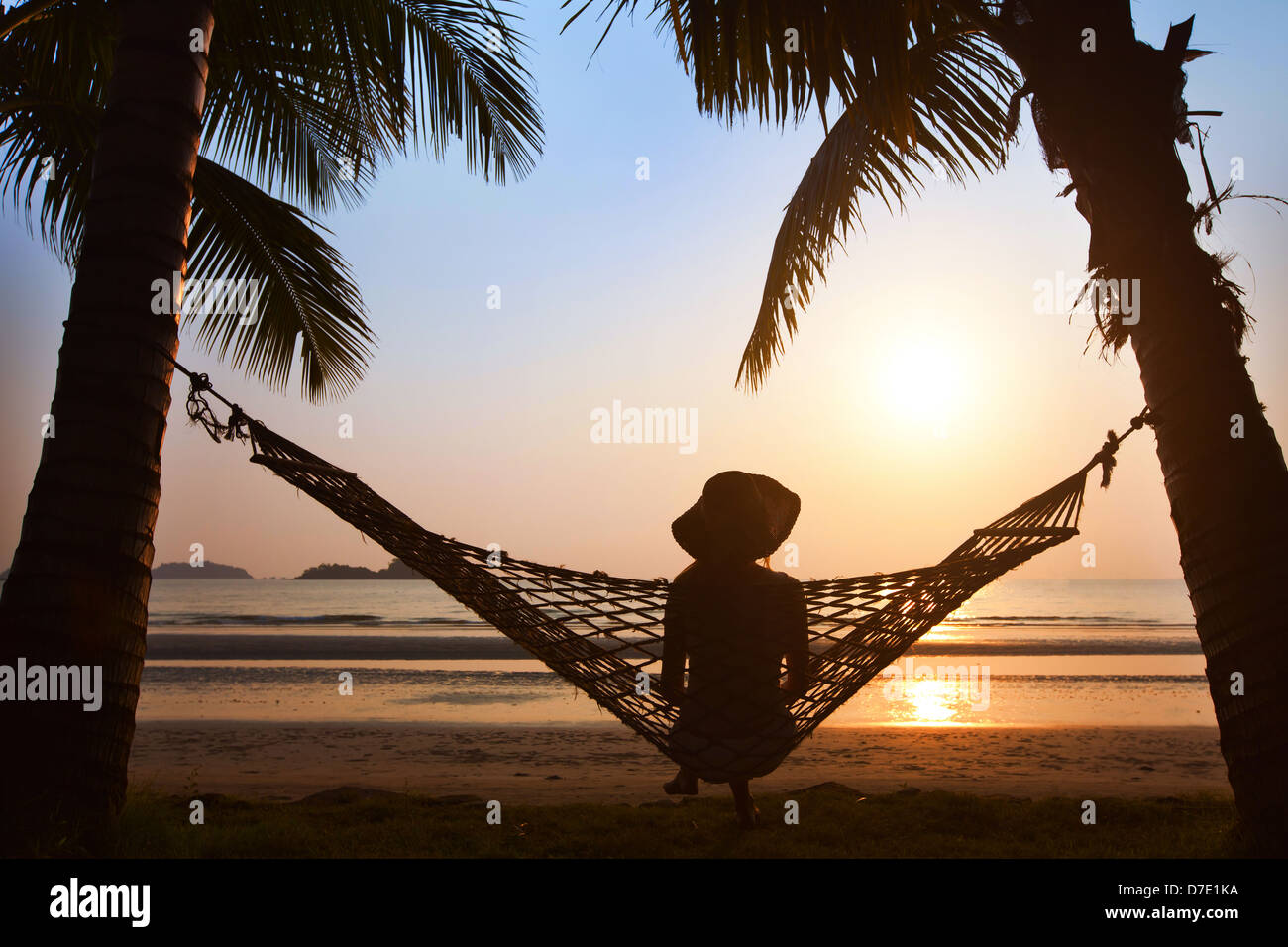 Silhouette di donna in hat in seduta amaca al tramonto sulla spiaggia Foto Stock