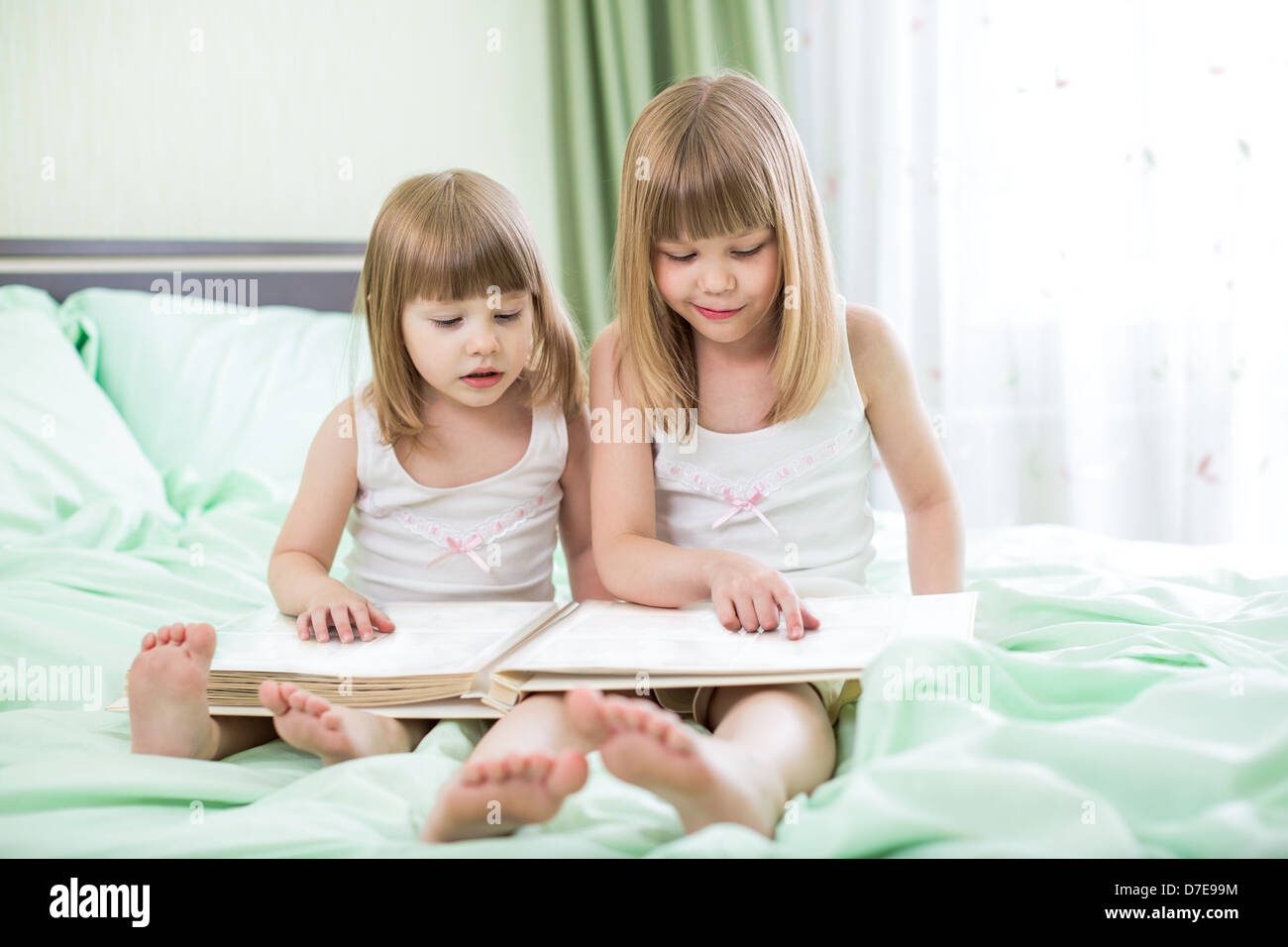 Due bambine lettura libro seduti sul letto Foto Stock