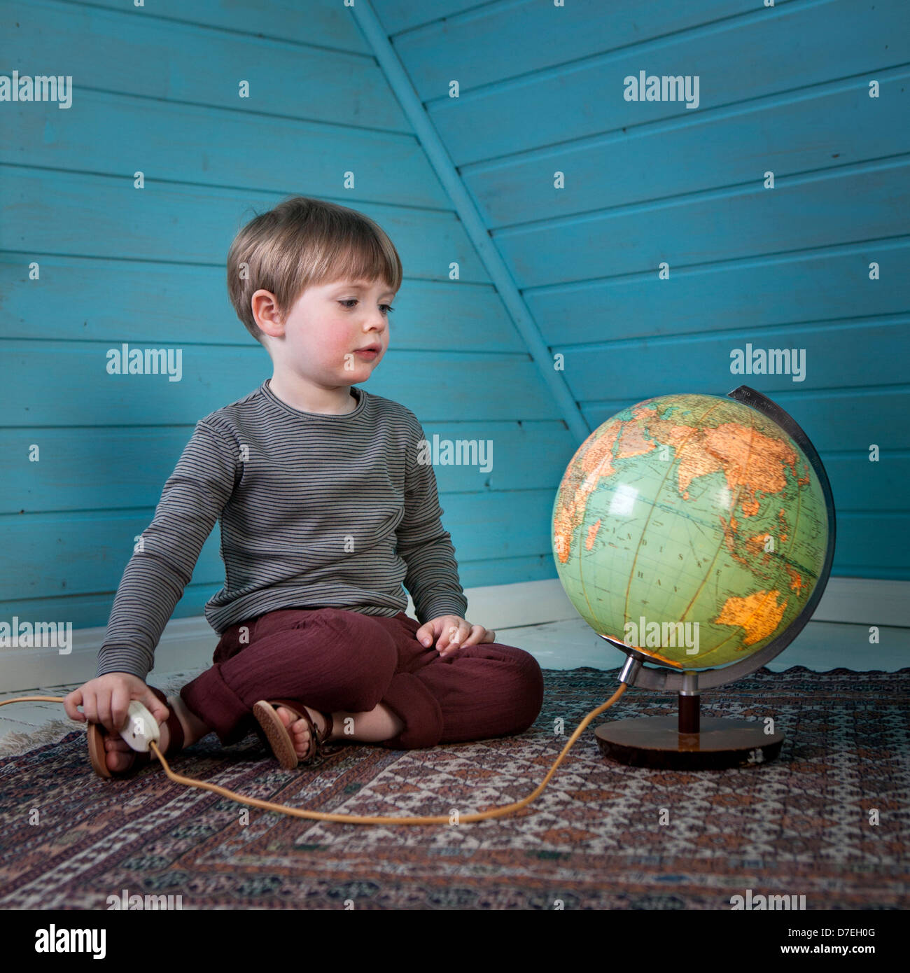 Un giovane bambino guarda un illuminato di globe pensando di luoghi lontani seduti in un accogliente attico a casa di luce Foto Stock