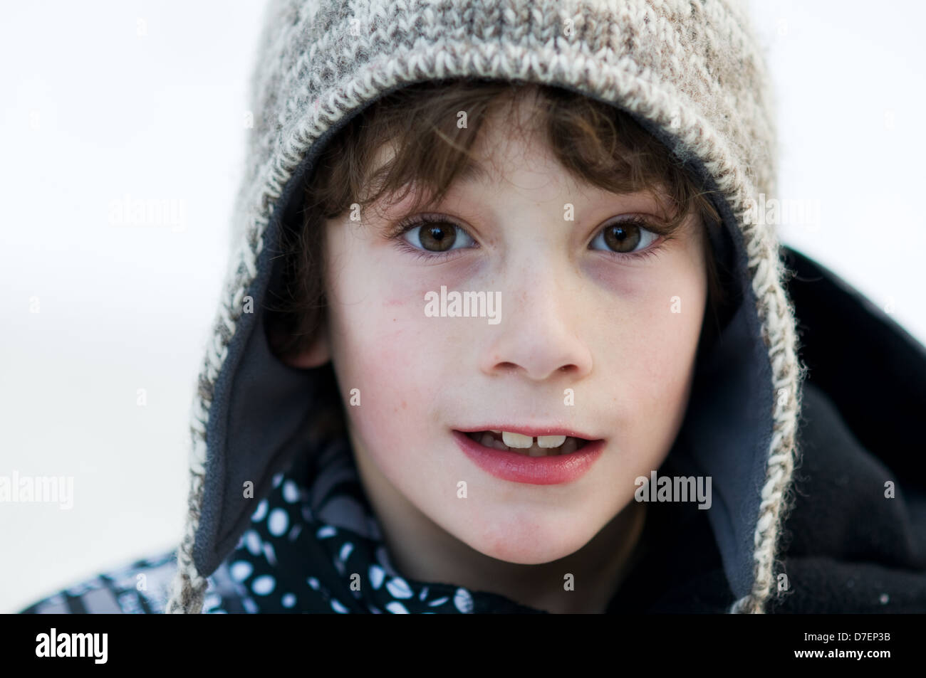 Close up di un bambino di otto anni che indossa un vago inverno hat all'aperto nella neve Foto Stock