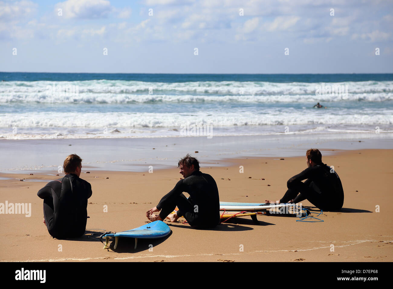 Tre surfers seduto sulla spiaggia Amado, Costa Vicentina, Portogallo Foto Stock