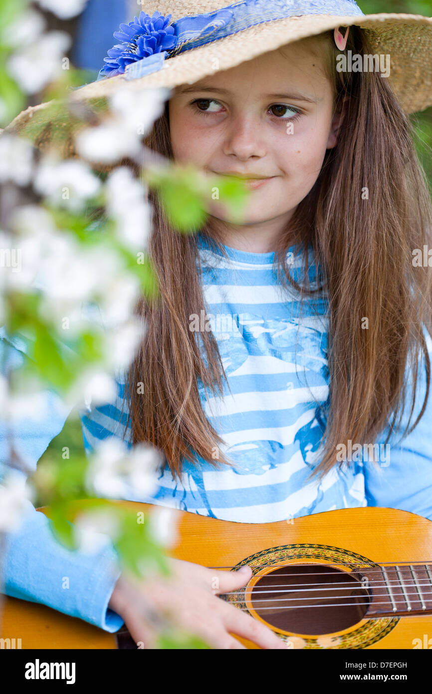 Ritratto di una ragazza con un cappello di paglia suonare la chitarra acustica nel giardino di primavera. Foto Stock