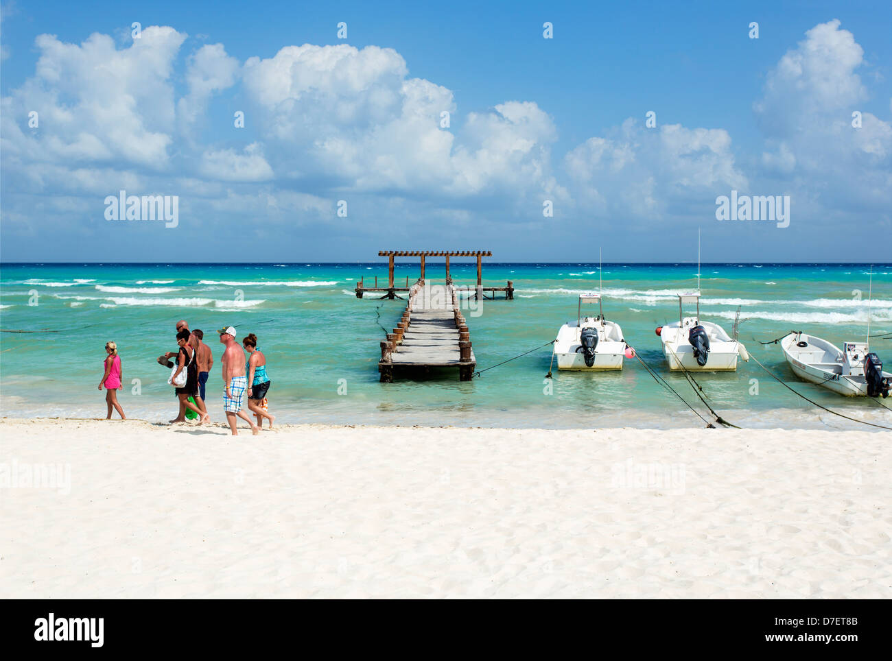 Gruppo di turisti in spiaggia a piedi passato un molo e barche da pesca. Foto Stock