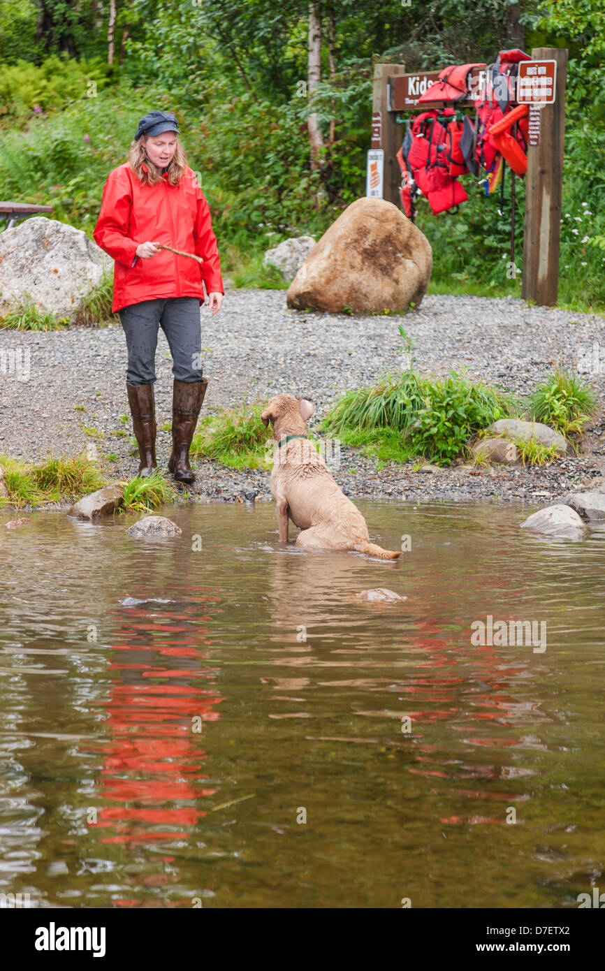 Donna che mantiene un bastone per gettare per un maschio chesepeak bay retriever chi è in attesa di recuperare, byers lago campeggio, Alaska Foto Stock