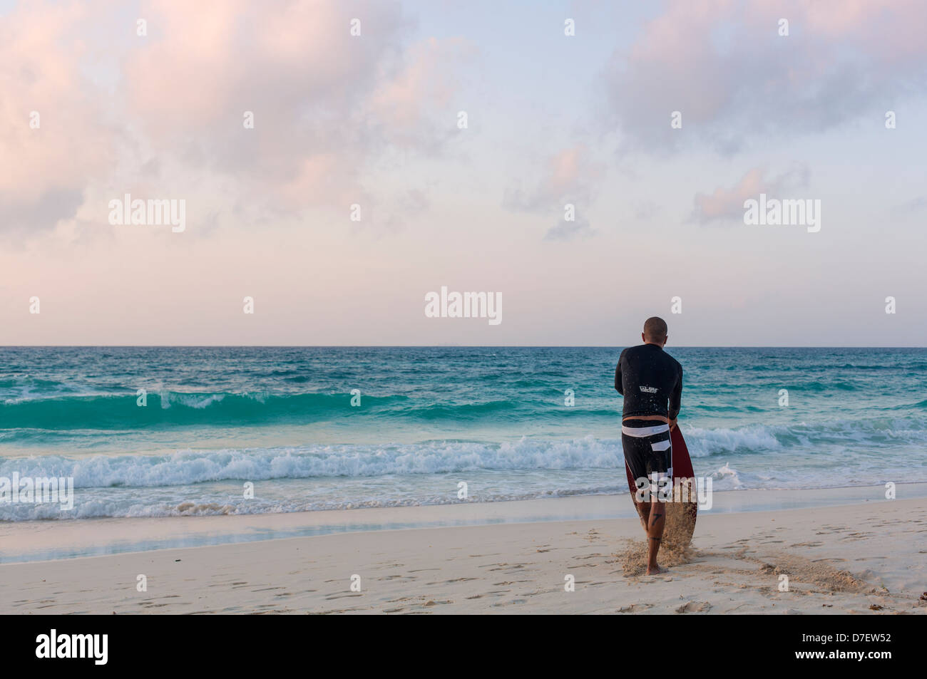 Surfista maschio in piedi su una spiaggia e si affaccia sul mare Foto Stock