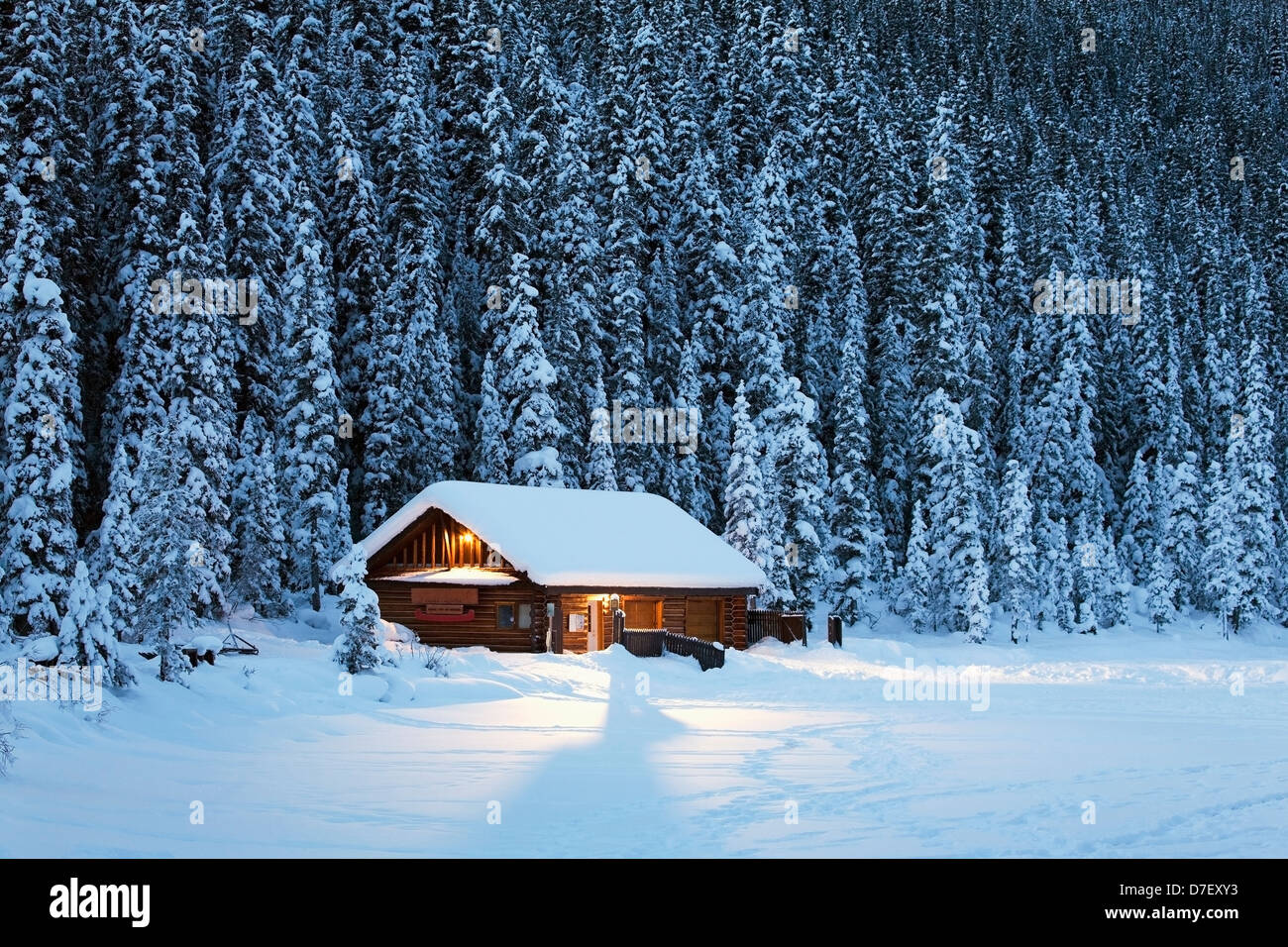 Una coperta di neve log cabin su una coperta di neve a lago circondato da alberi sempreverdi al crepuscolo;Lake Louise Alberta Canada Foto Stock