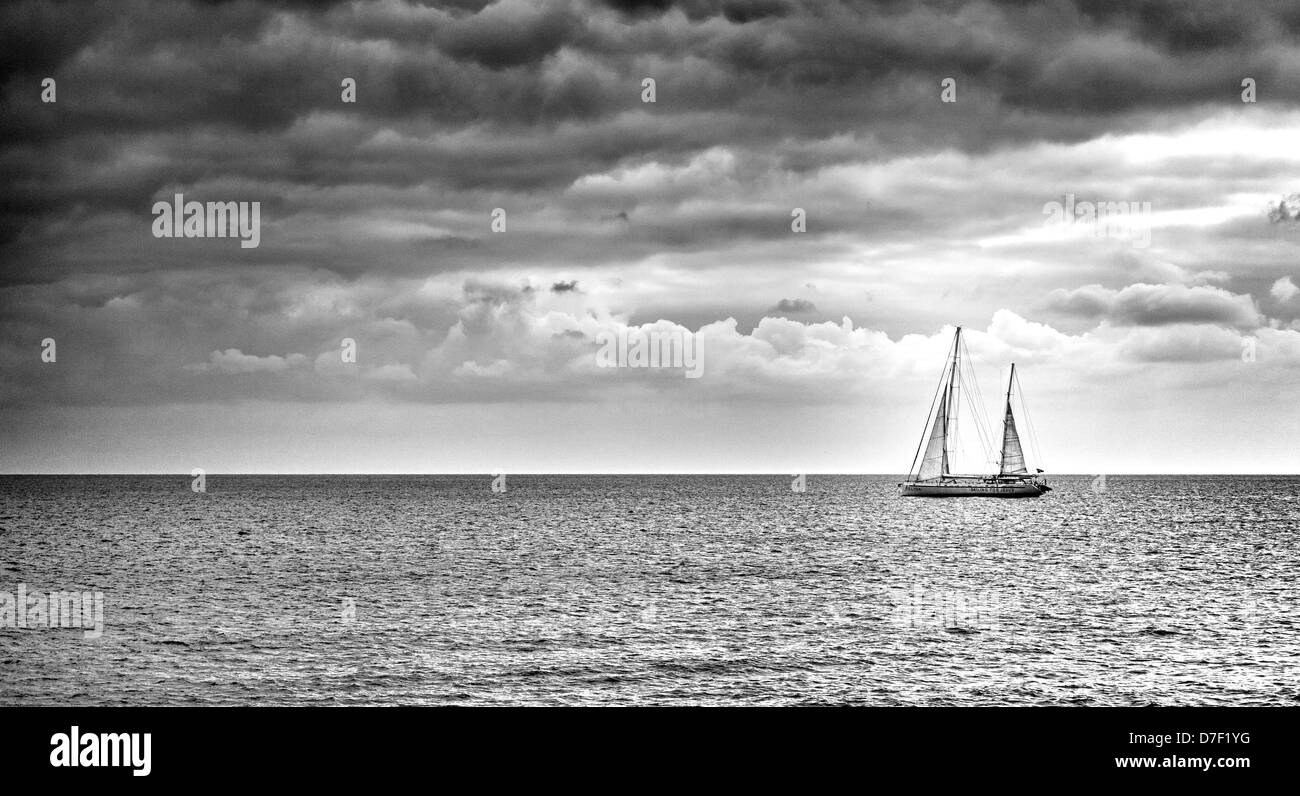 Barca a vela illuminato dai raggi di sole su un mare calmo vela verso le nuvole Foto Stock