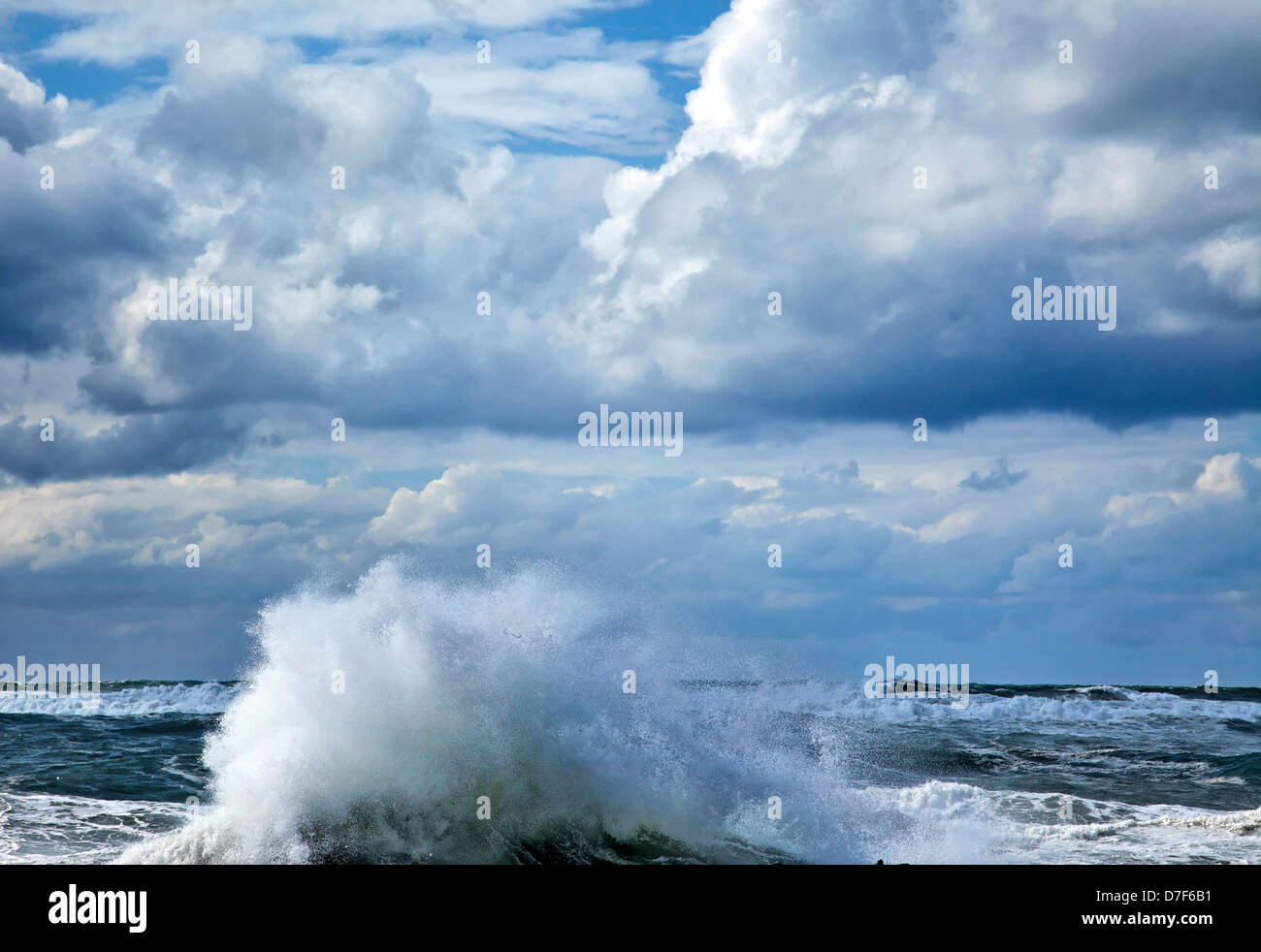 Un onda gigante di innalzarsi al di sopra del mare acqua affiorato il suo surf diffusa dal forte vento sotto pesantemente nuvoloso cielo d'inverno. Foto Stock