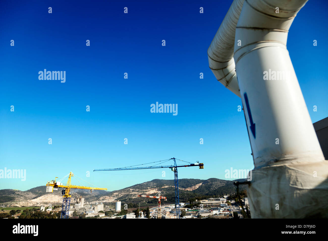 Tetto a tubazioni di acqua in primo piano dietro la parte superiore delle gru a torre innalzarsi al di sopra di un parco industriale situato in un ambiente rurale. Foto Stock