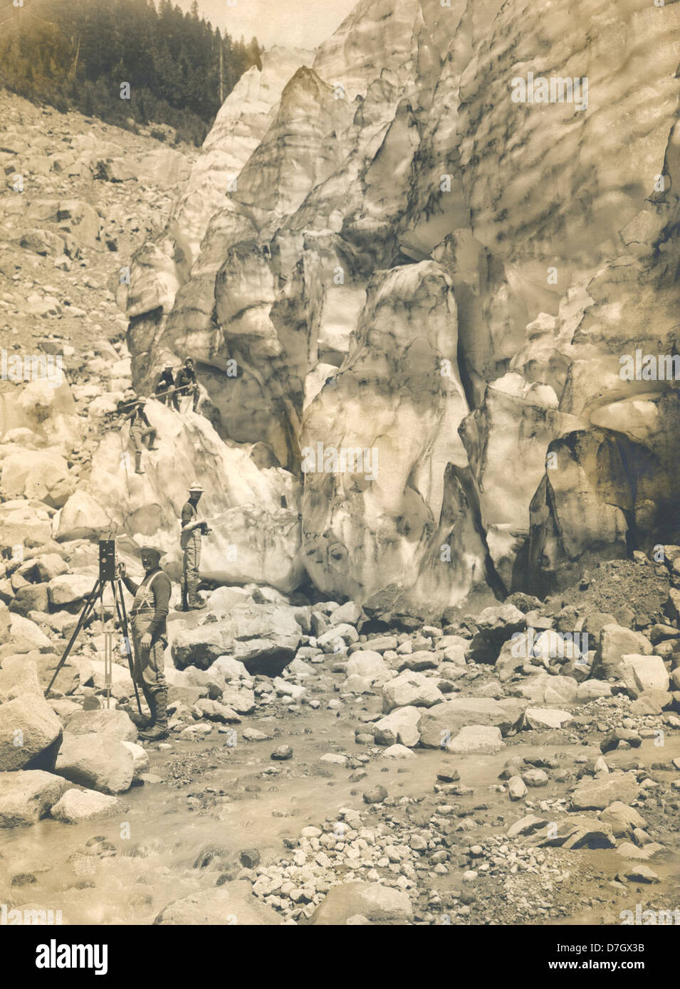Questa immagine cattura un uomo che filma vicino a un ghiacciaio al Monte Rainier, evidenziando l'intersezione tra la natura e la prima tecnologia cinematografica. La scena fa parte della collezione Gerald W. Williams, che espone fotografie all'aperto e alpinismo. Foto Stock