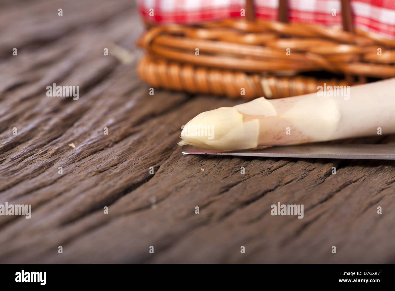 Ripresa macro di una punta di asparagi con un coltello su un rustico sfondo di legno fuori fuoco sullo sfondo di un piccolo carrello Foto Stock