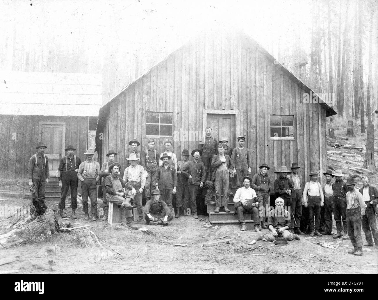 Una fotografia storica in bianco e nero raffigurante i taglialegna in piedi di fronte a un edificio del campo di taglialegna. L'immagine riflette la vita dei taglialegna all'inizio del XX secolo e il paesaggio industriale del disboscamento in Nord America. Foto Stock