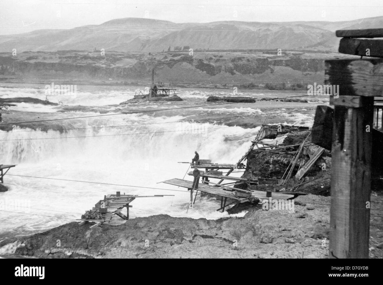 Questa fotografia storica mostra un uomo che pesca su una piattaforma alle Celilo Falls sul fiume Columbia. L'immagine cattura il significato delle cascate, un importante sito di pesca per le tribù indigene del nord-ovest del Pacifico, e mette in evidenza i metodi di pesca tradizionali utilizzati nella zona. Foto Stock