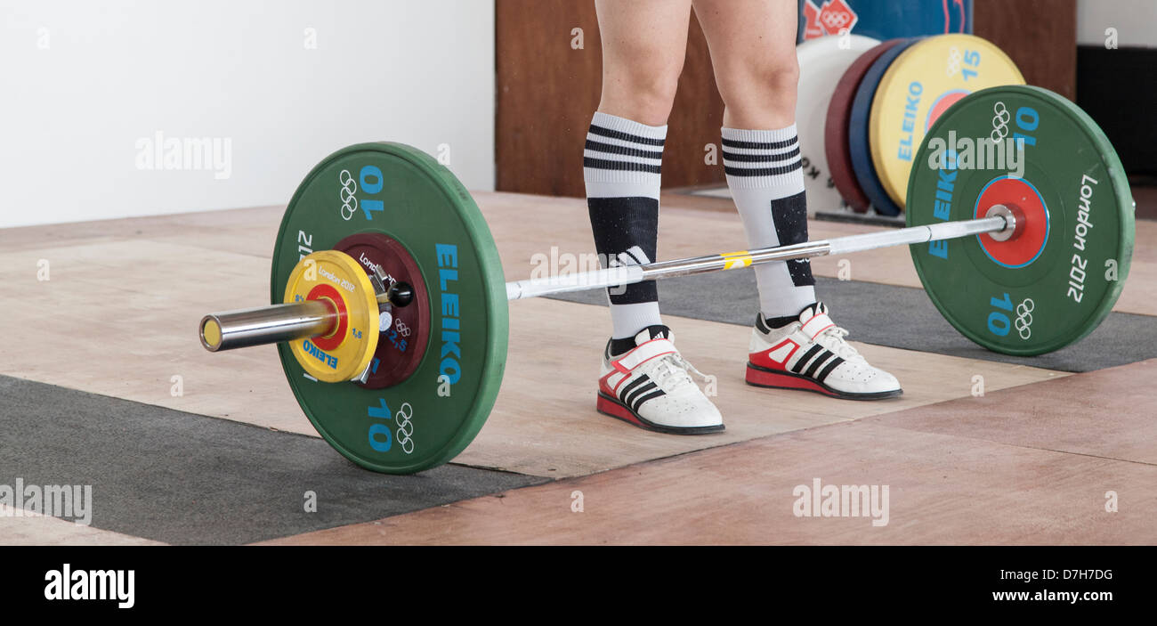 Gambe di weightlifter standing, pronto a sollevare la barra olimpici di Londra con piastre 2012. Foto Stock