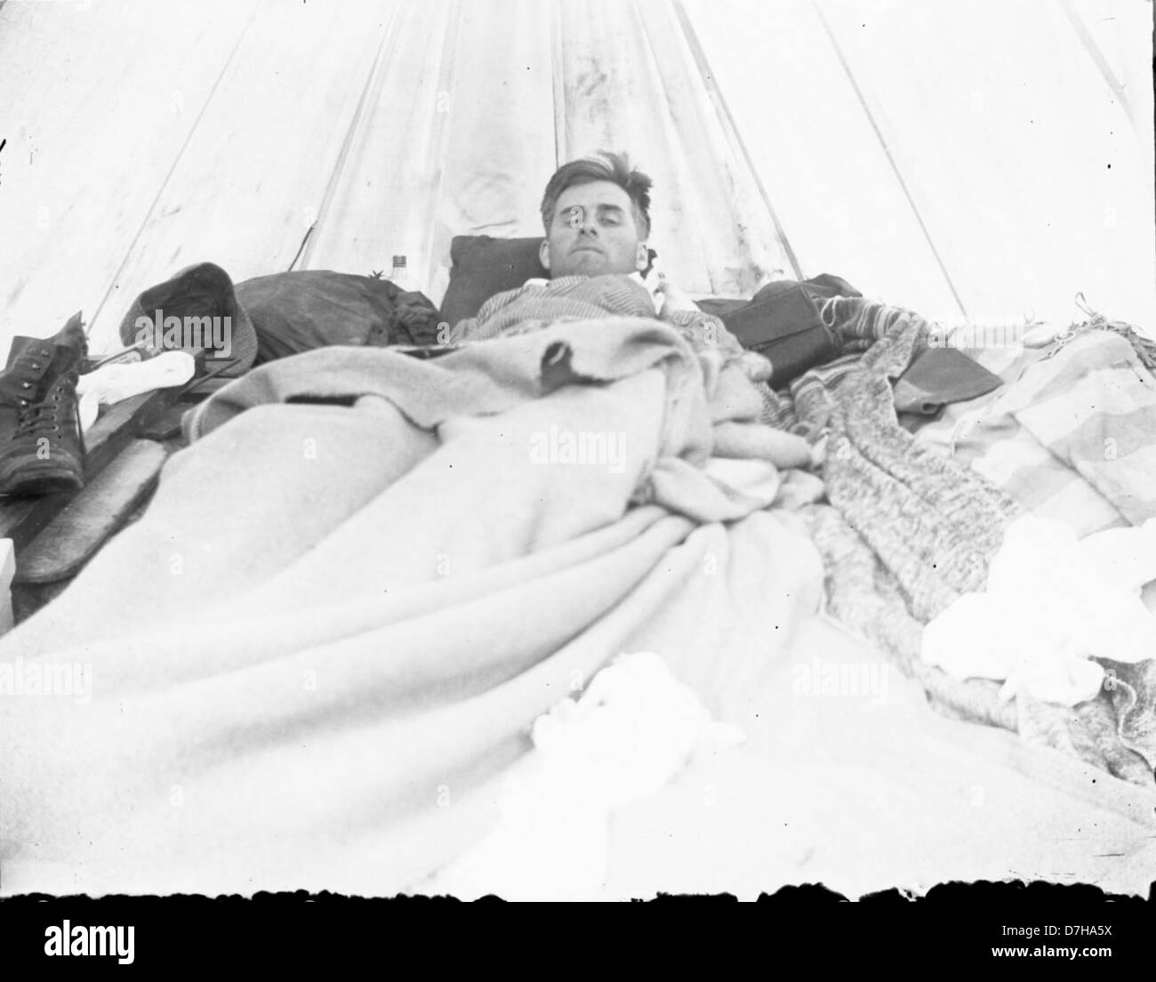 Questa fotografia, parte della collezione Herman Bohlman, mostra un uomo che dorme all'interno di una tenda, sottolineando la semplicità e la solitudine della vita in campeggio. L'immagine cattura un momento tranquillo di vita all'aperto. Foto Stock