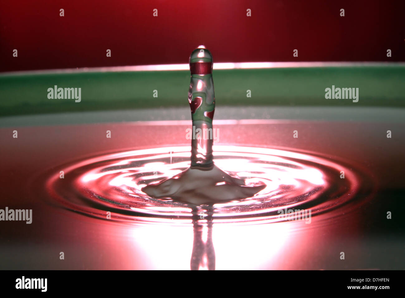 Una goccia di acqua che hanno acqua rosso e verde dello sfondo. Foto Stock