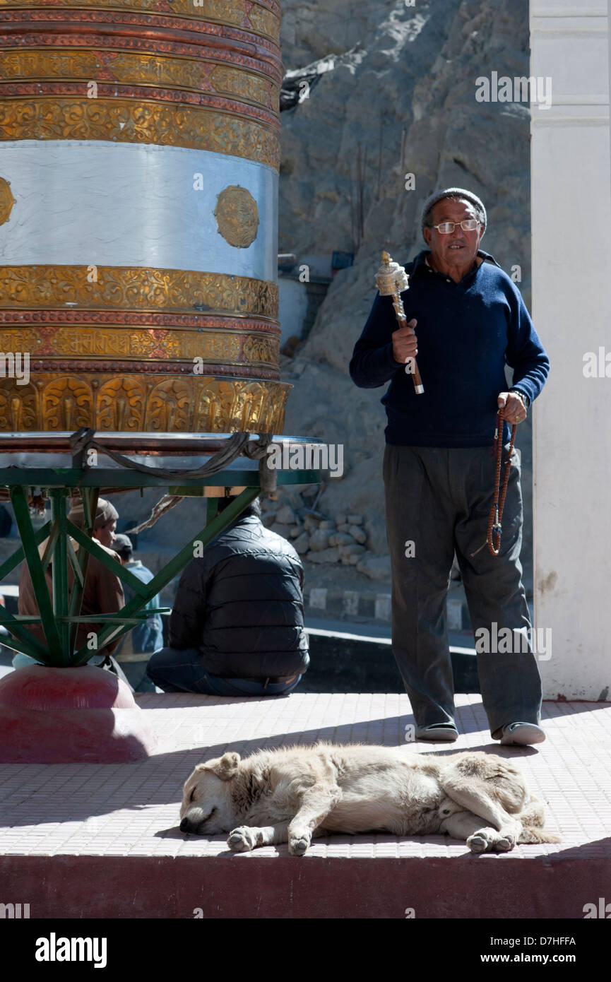 Un buddista uomo con ruota di preghiera e la preghiera di perline in mano, passeggiate intorno ad un enorme oro ruota di preghiera in Leh-Ladakh. India Foto Stock