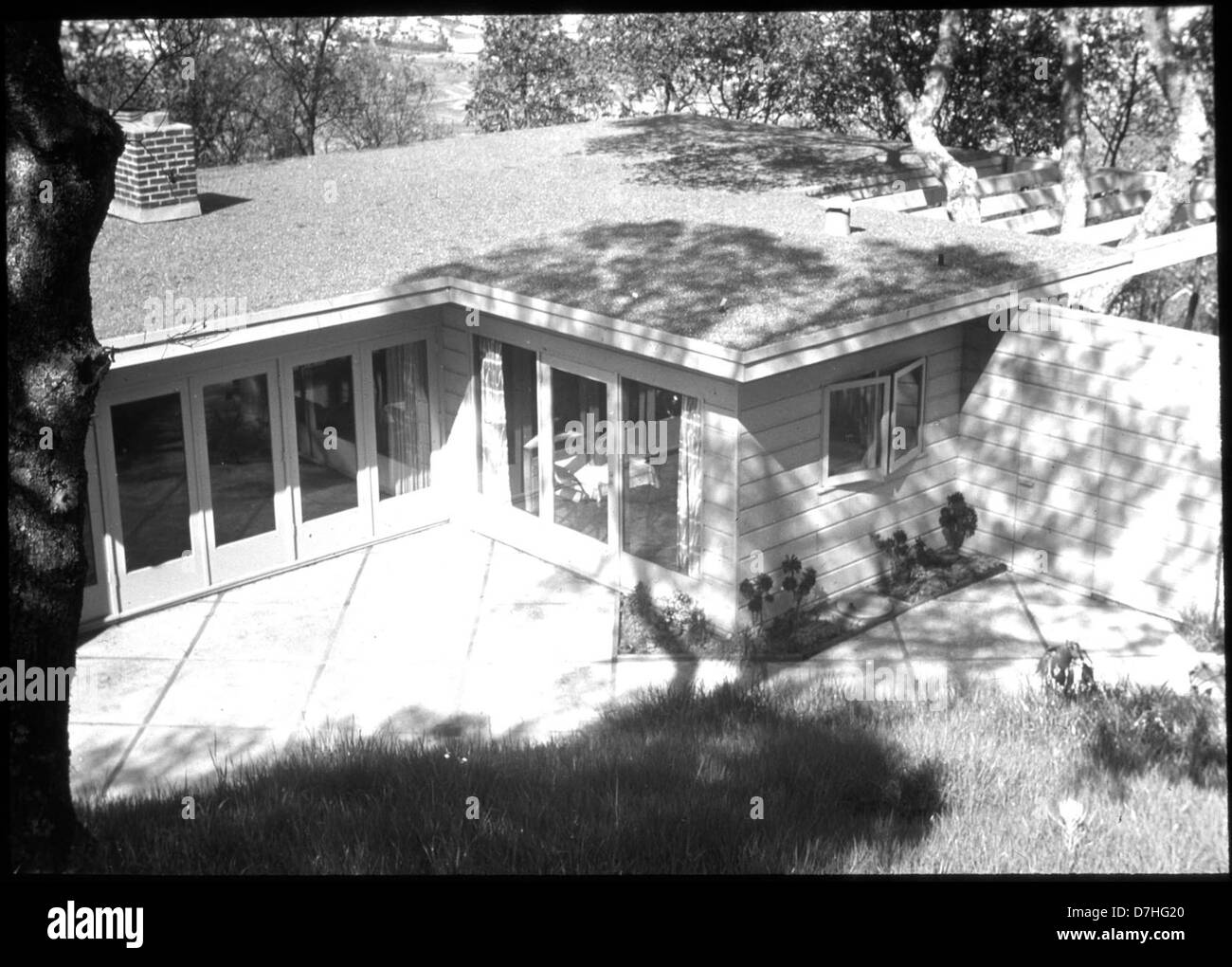 Una casa dal tetto piatto è vista da una collina, che mostra il design architettonico moderno della struttura, con un cortile e uno spazio patio visibile sotto. Foto Stock