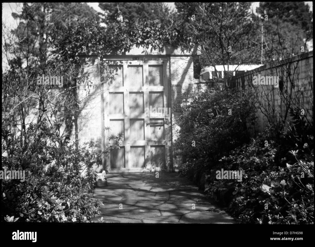 Immagine di un sentiero in pietra che conduce ad un cancello, con una porta alla fine che può condurre ad un giardino segreto o ad una fermata dell'autobus dall'altro lato. L'immagine gioca con la prospettiva, catturando un'ambientazione architettonica intrigante. Foto Stock