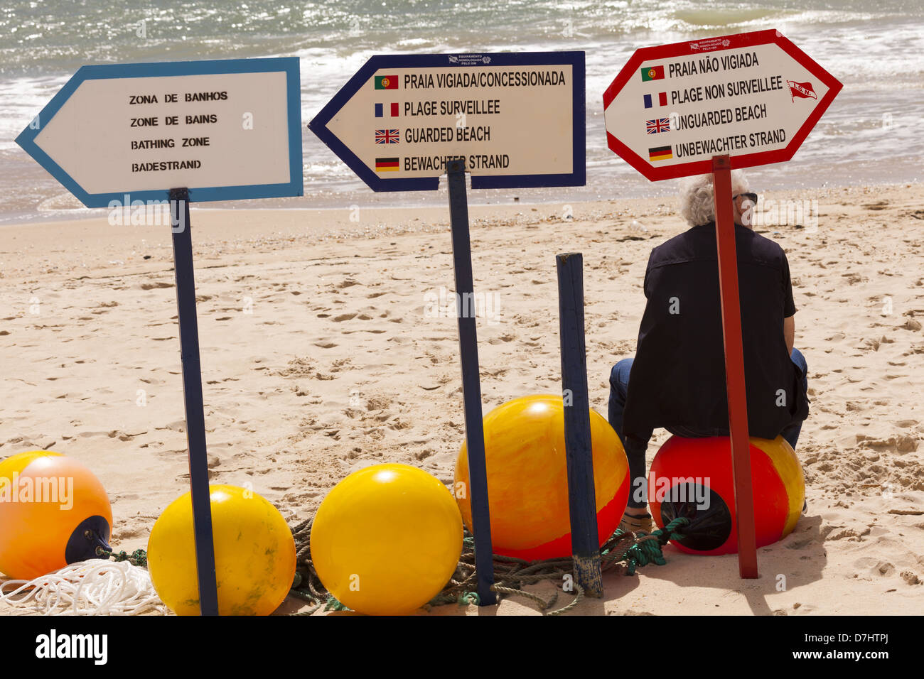 Lone man by Beach avvisi di sicurezza con una fila di pesca colorata e luminosa galleggia con un uomo seduto su di loro. Tavira Portogallo. Foto Stock