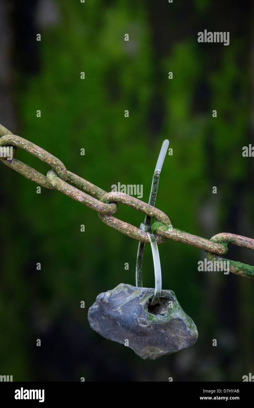 Una piccola pietra con un foro in esso il filo-legato a una catena di ruggine. Foto Stock