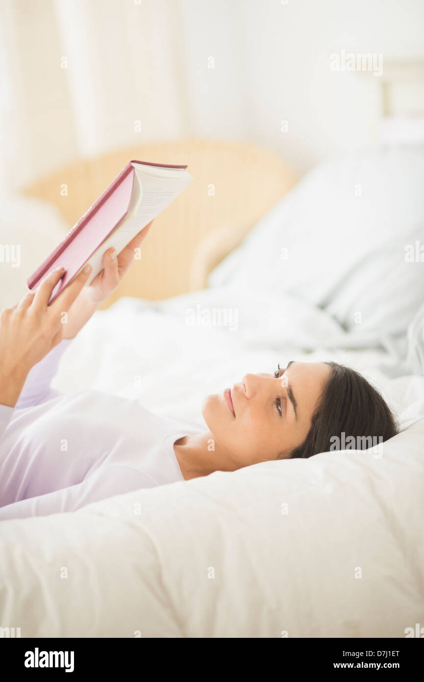 Donna giaceva a letto e un libro di lettura Foto Stock
