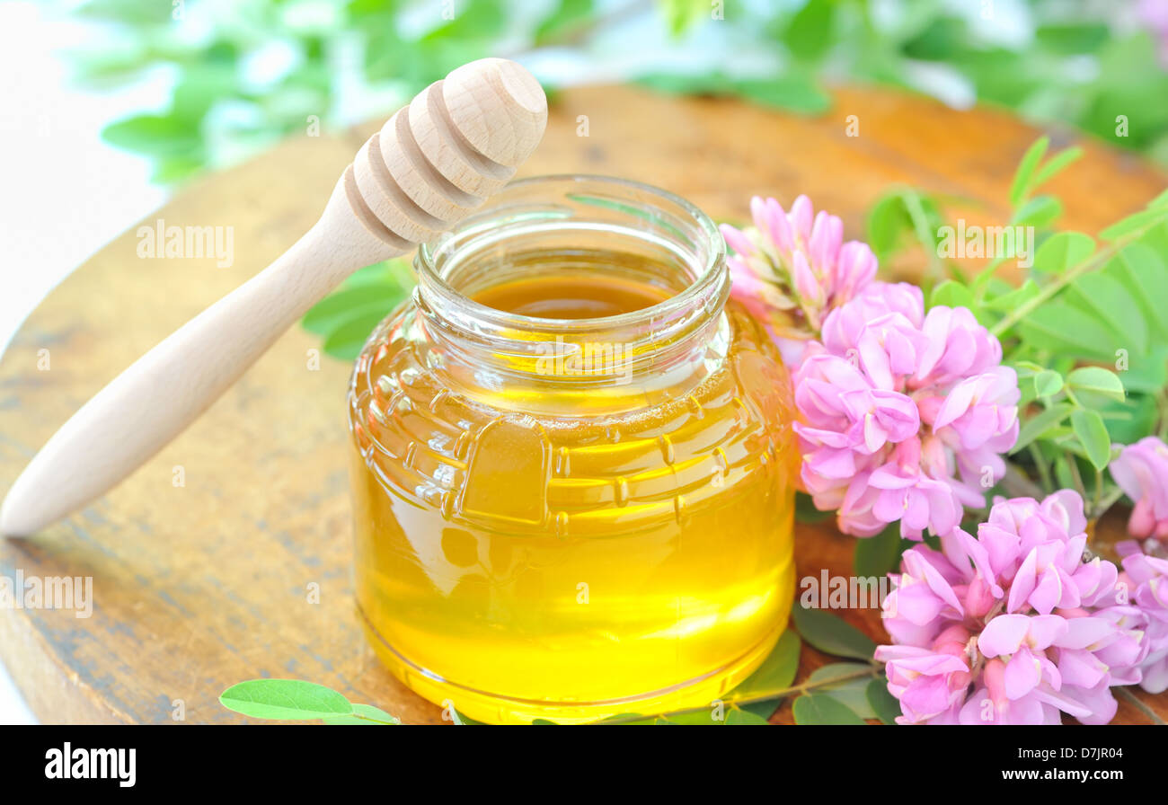 Vaso pieno di miele e stick con acacia fiori rosa e bianchi Foto Stock