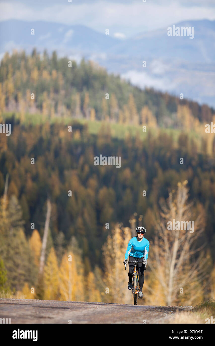 Stati Uniti d'America, Montana, coregoni, Donna ciclismo su rurale strade di montagna in autunno Foto Stock