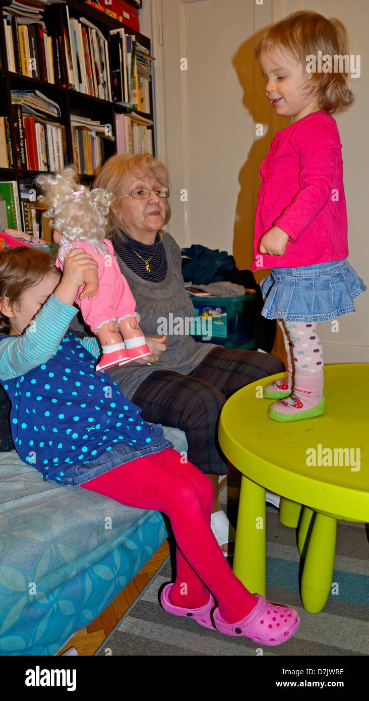 Senior donna che gioca con i suoi due piccolo nipote a casa. Il bambino di 2 anni in piedi sulla tavola Foto Stock
