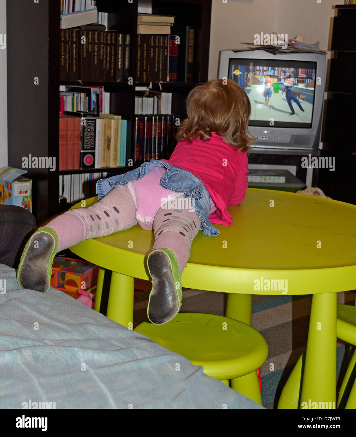 Bambina giacente sul tavolo di guardare la televisione, vista posteriore Foto Stock