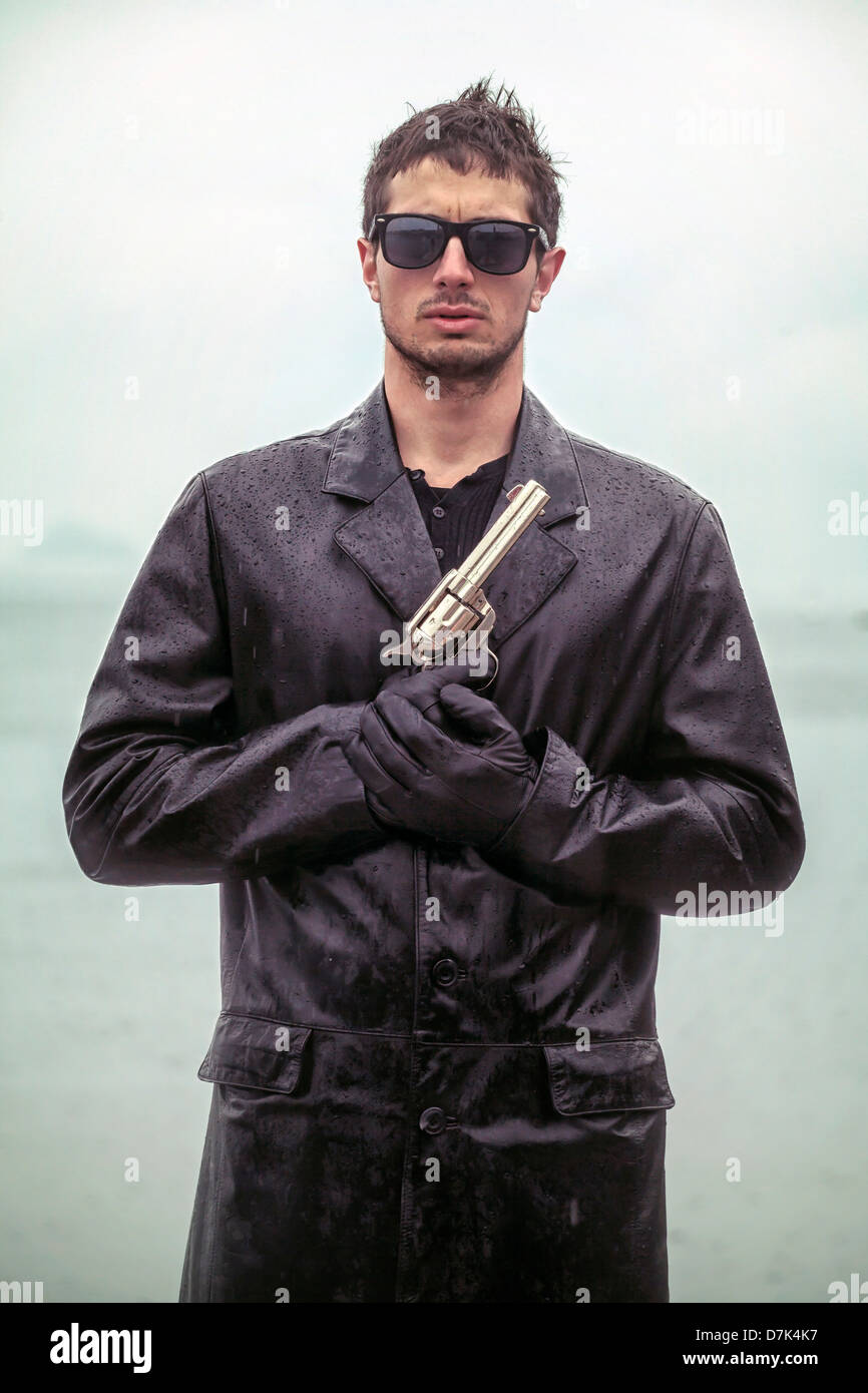 Un uomo in nero, wet giacca di pelle con una pistola Foto Stock