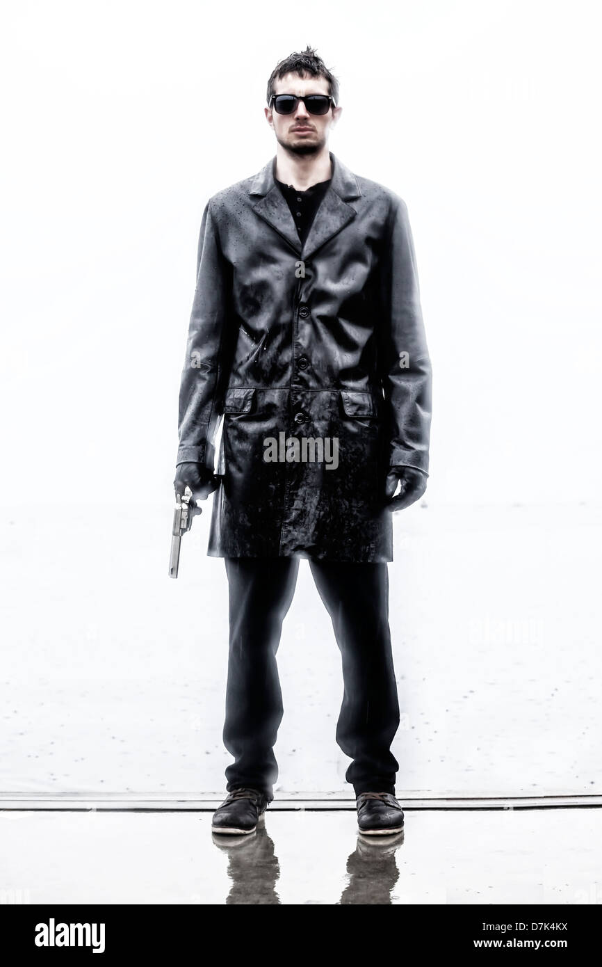 Un uomo in nero, wet giacca di pelle con una pistola Foto Stock