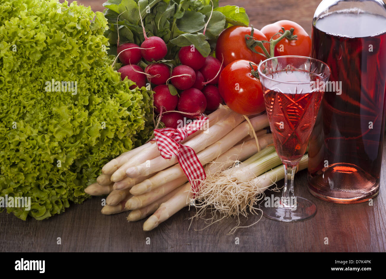 Ortaggi freschi con asparagi e insalata su uno sfondo di legno e un bicchiere di vino rosato Foto Stock