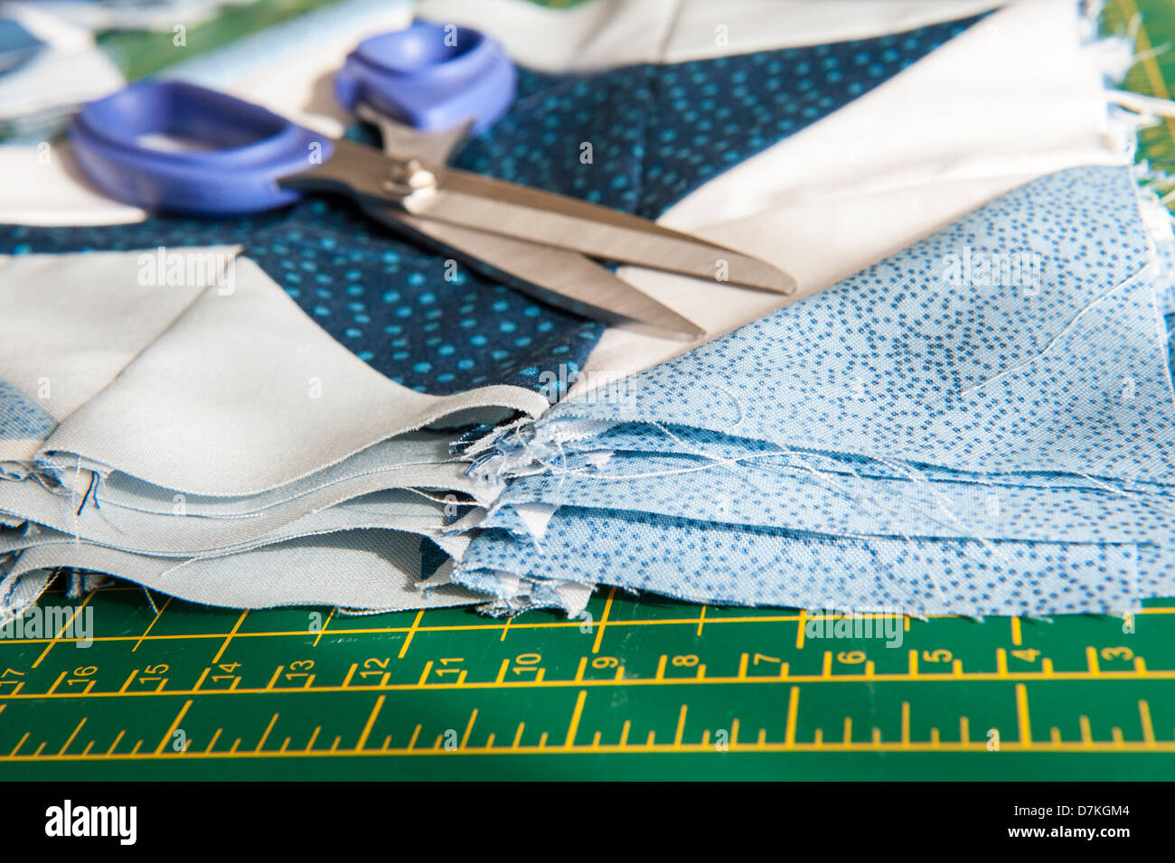 La trapuntatura o un patchwork di materiali e strumenti su un verde scheda di misura con le forbici che mostra blu e bianco modellato fat quarters Foto Stock