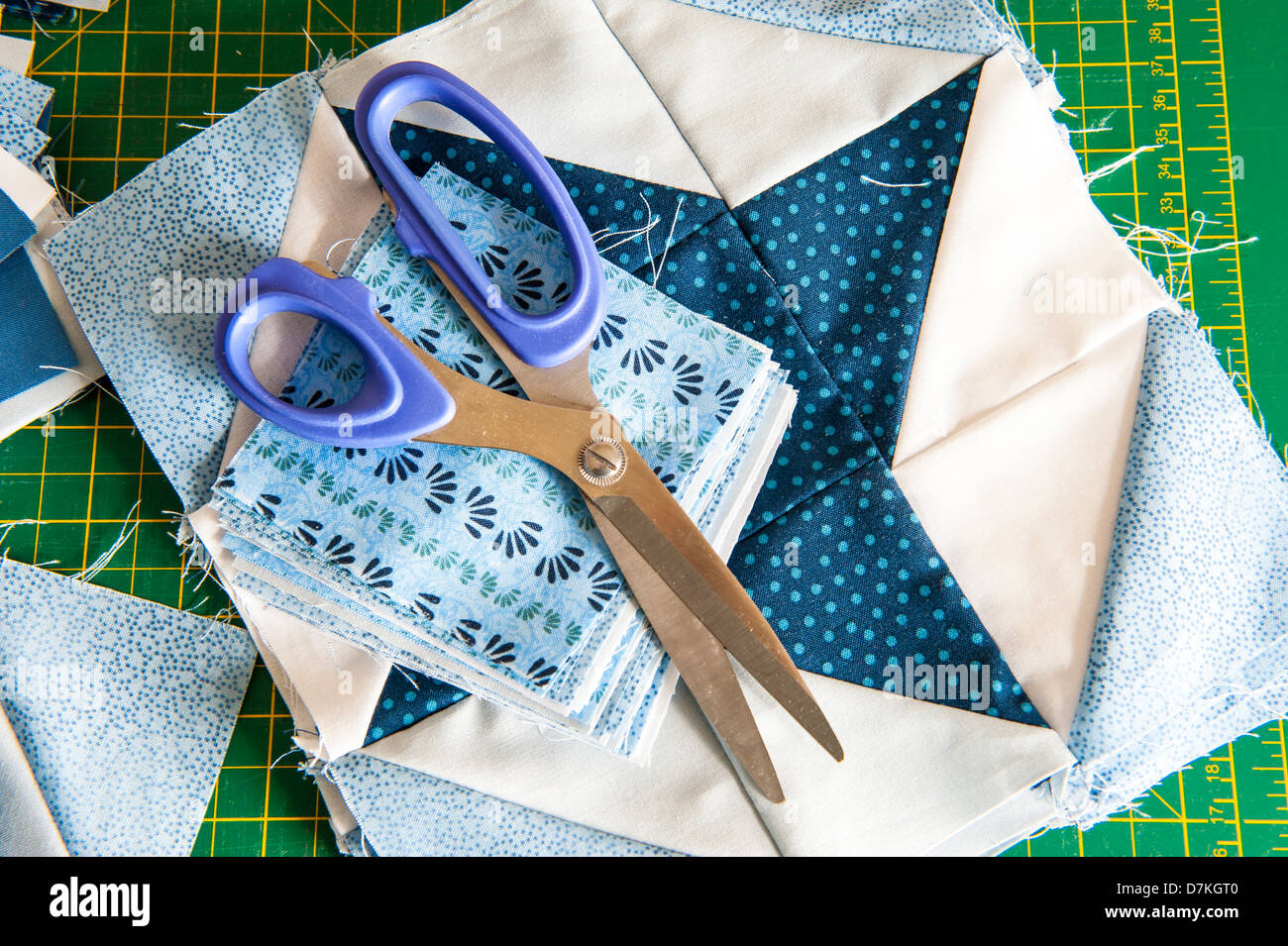 La trapuntatura o un patchwork di materiali e strumenti su un verde scheda di misura con le forbici che mostra blu e bianco modellato fat quarters Foto Stock