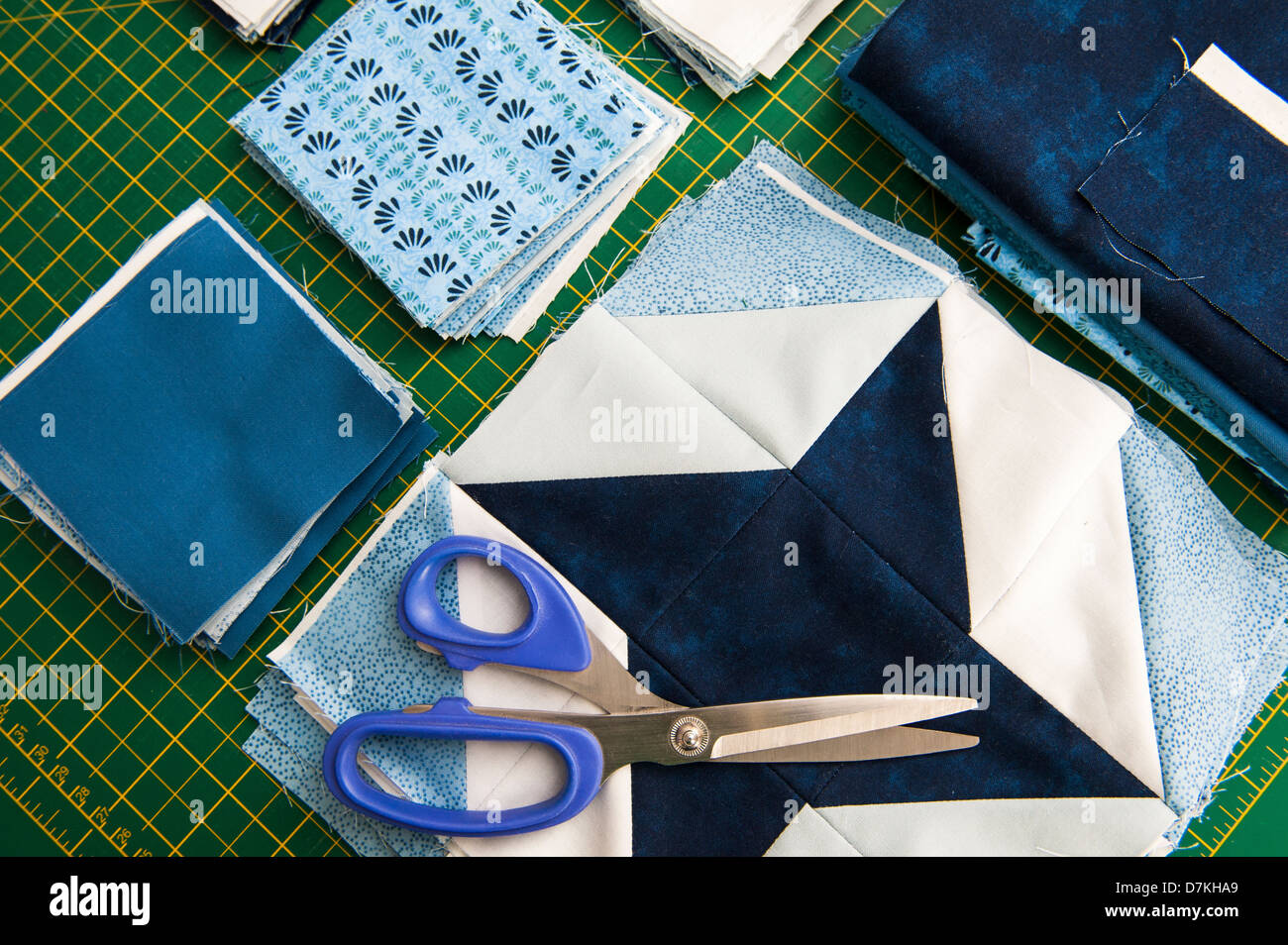 La trapuntatura o un patchwork di materiali e strumenti su un verde scheda di misura con le forbici che mostra blu e bianco modellato fat quarters Foto Stock